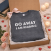 A sweatshirt in a gift box that says 'Go away Im reading'