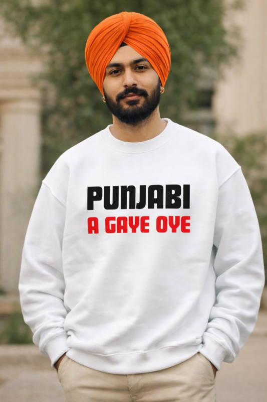 “A young Indian man with a neatly tied orange turban and trimmed beard stands outdoors wearing a white sweatshirt that reads ‘PUNJABI’ in bold black letters and ‘A GAYE OYE’ in bold red letters. He looks confidently at the camera with his hands in his pockets.”