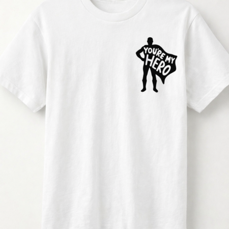 White short‑sleeved T‑shirt laid flat on a light background featuring a small black superhero silhouette logo on the front left chest with the words “YOU’RE MY HERO” inside the cape.